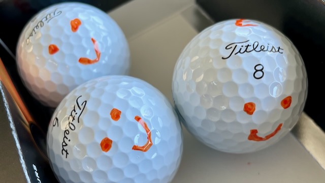 Golf balls marked up with orange smiley faces